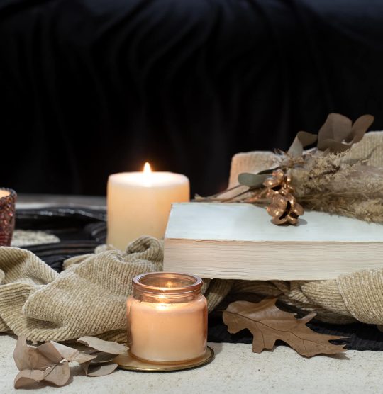 still-life-table-book-candle-tea-space-dark-sofa-autumn-coziness-concept